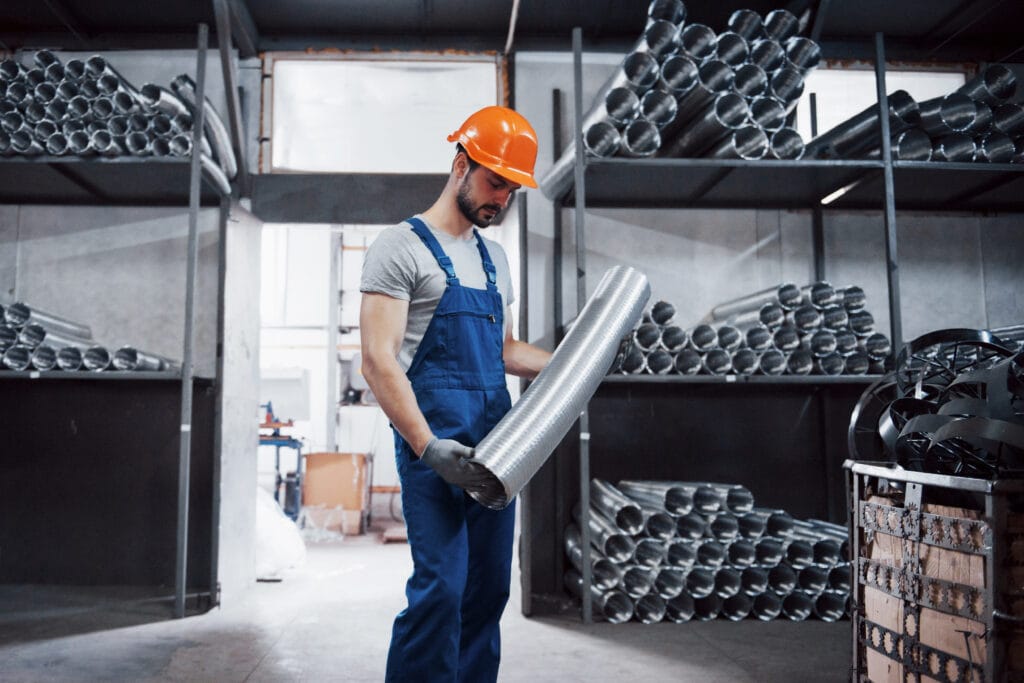 Portrait of a young worker in a hard hat at a large metalworking plant. Shiftman on the warehouse of finished products