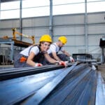 Industrial workers working in factory hall with metal.